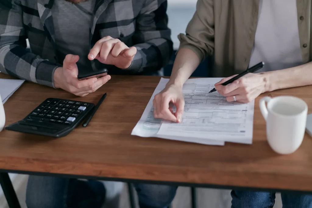 Two people working through financial paperwork with a calculator at a desk