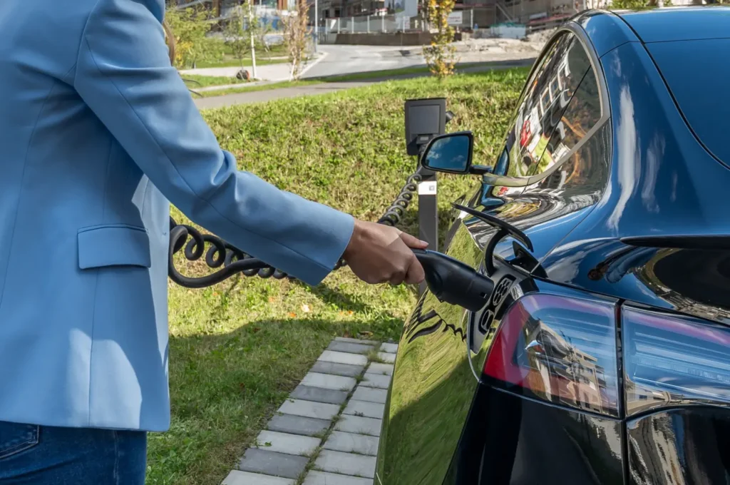 A person in business attire plugging a charging cable into an electric vehicle