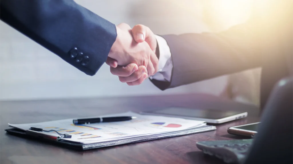 Two people shaking hands over a clipboard of financial charts