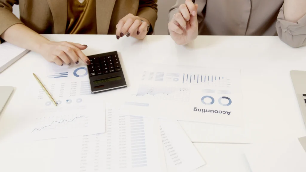 Two people reviewing printed accounting reports with a calculator on a white desk